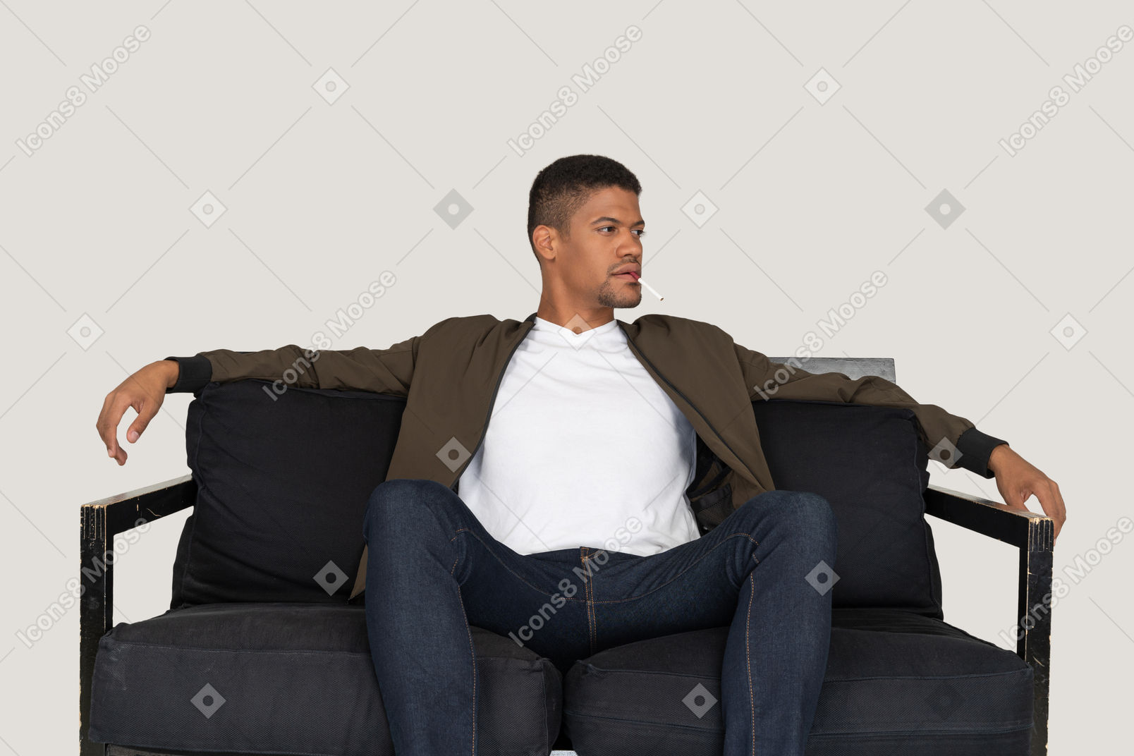 Вид спереди молодого человека, сидящего на диване и держащего сигарету во рту