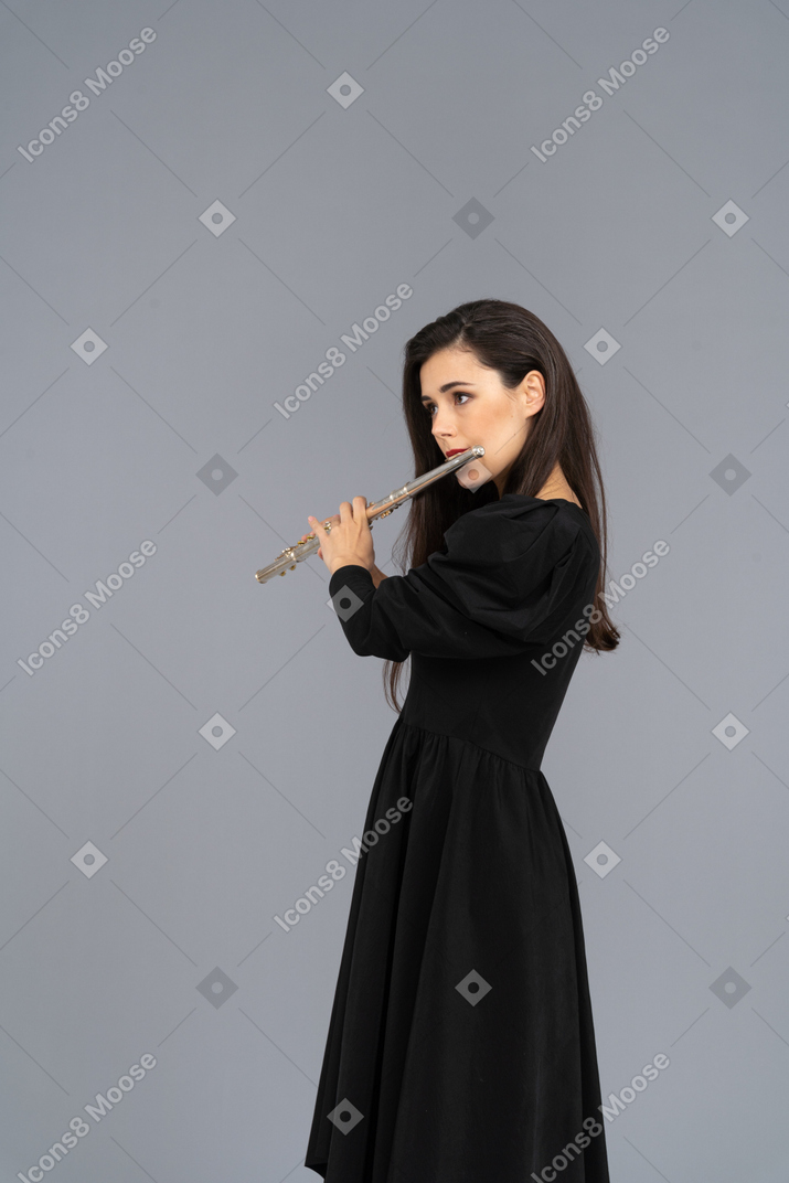 Three-quarter view of a serious young lady in black dress playing the flute