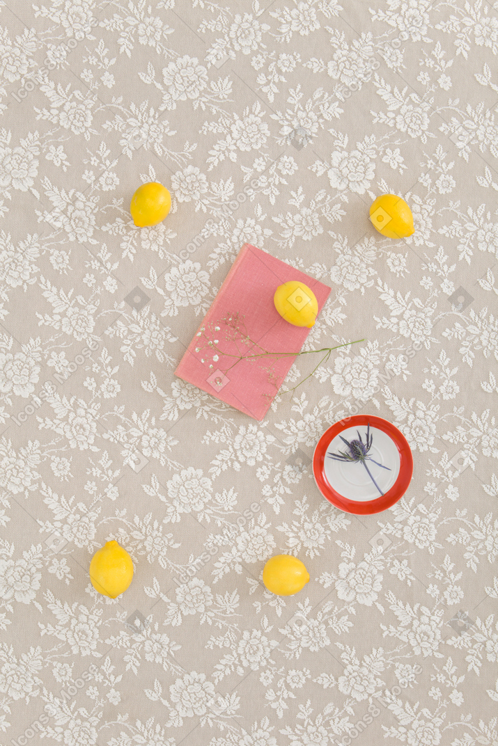 Zitronen, rosa buch und trockenblumen auf einer tischdecke mit blumendesign