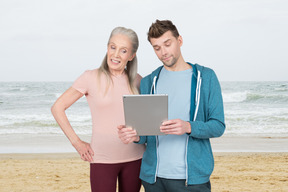 A man and a woman looking at tablet on a beach