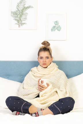 Front view of an ill young lady wrapped in white blanket staying in bed