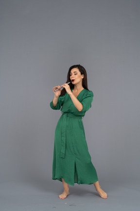 Vista frontale di una giovane donna in abito verde che suona il flauto