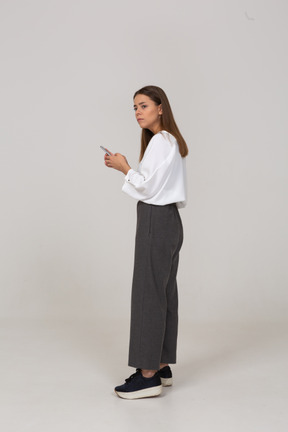 Vista lateral de uma jovem com roupas de escritório, verificando o feed por telefone