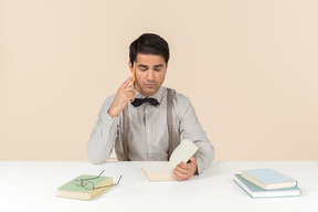 Pensive adult student sitting at the table with opened book