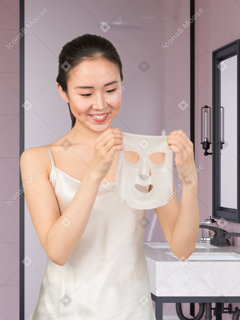 A woman is holding a skin care face mask in bathroom