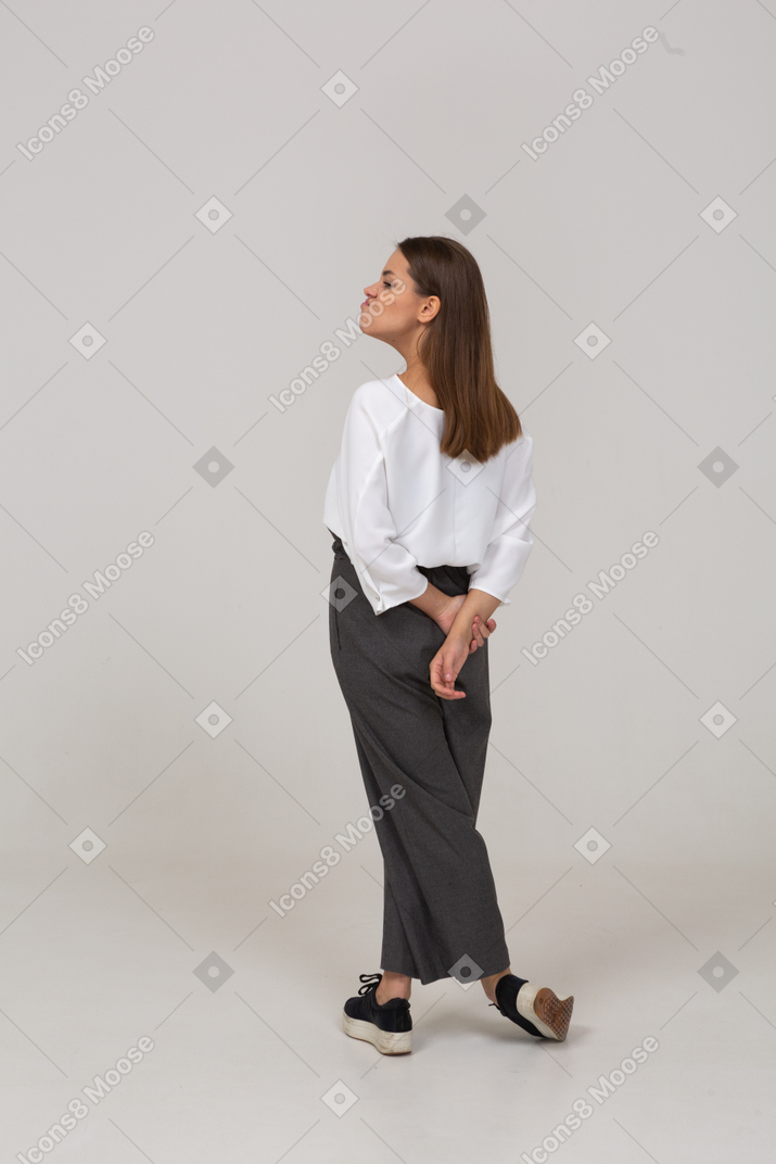 一个顽皮的年轻女士在办公室服装的后视图撅嘴和牵手在后面