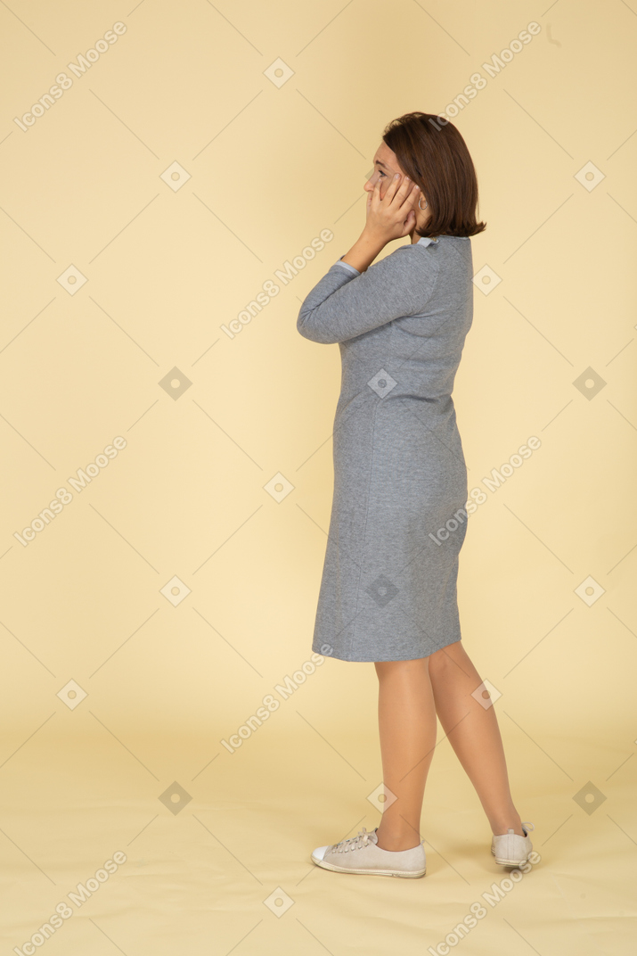 一个穿着灰色裙子的悲伤女人抚摸她的脸的侧视图