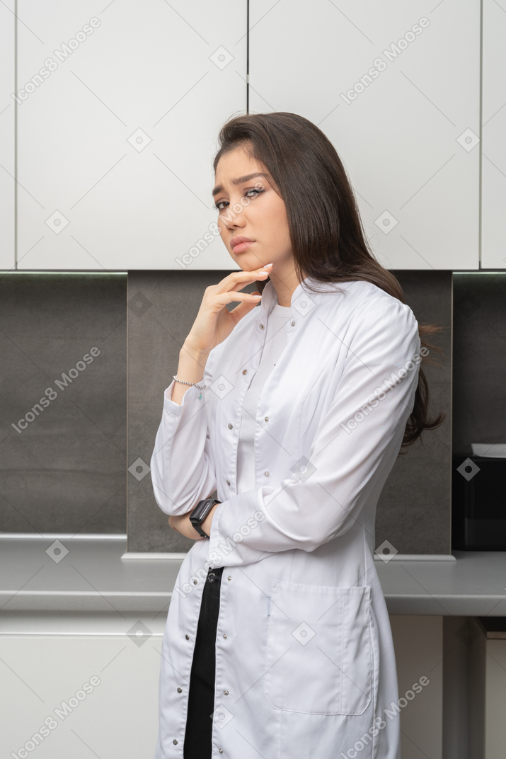 Three-quarter view of a suspicious female doctor looking at camera and touching chin