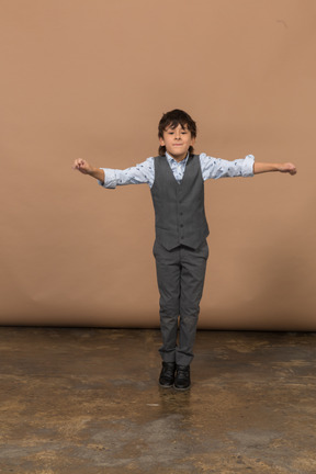 Вид спереди симпатичного мальчика в костюме, стоящего с протянутыми руками