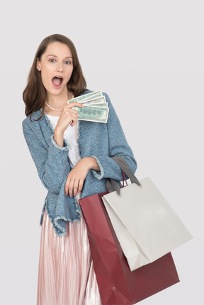Excited young girl holding shopping bags and money bills