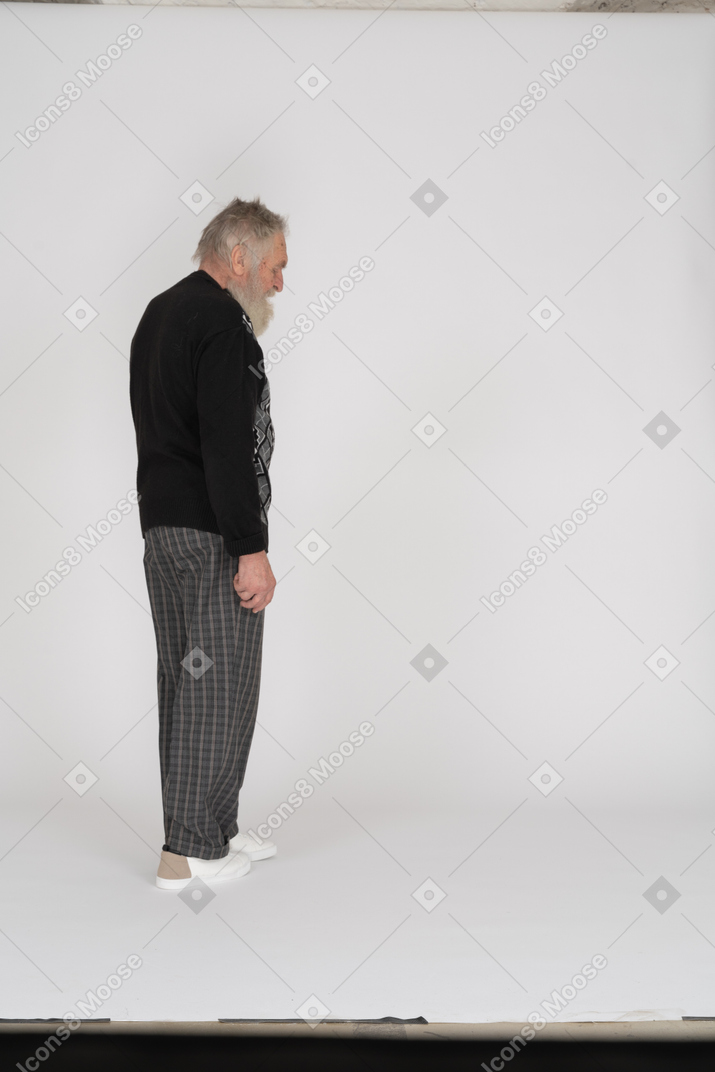 Vista lateral de un anciano caminando y mirando hacia abajo