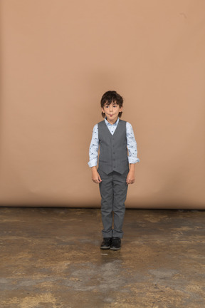 Vista frontal de un niño en traje parado y haciendo muecas