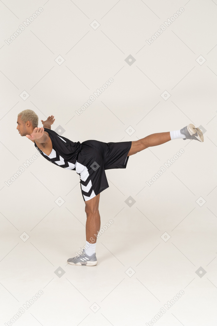 Side view of a balancing young male basketball player leaning forward & standing on one leg