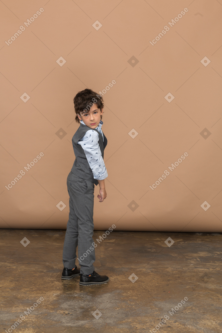 Вид сбоку на мальчика в сером костюме, смотрящего в камеру