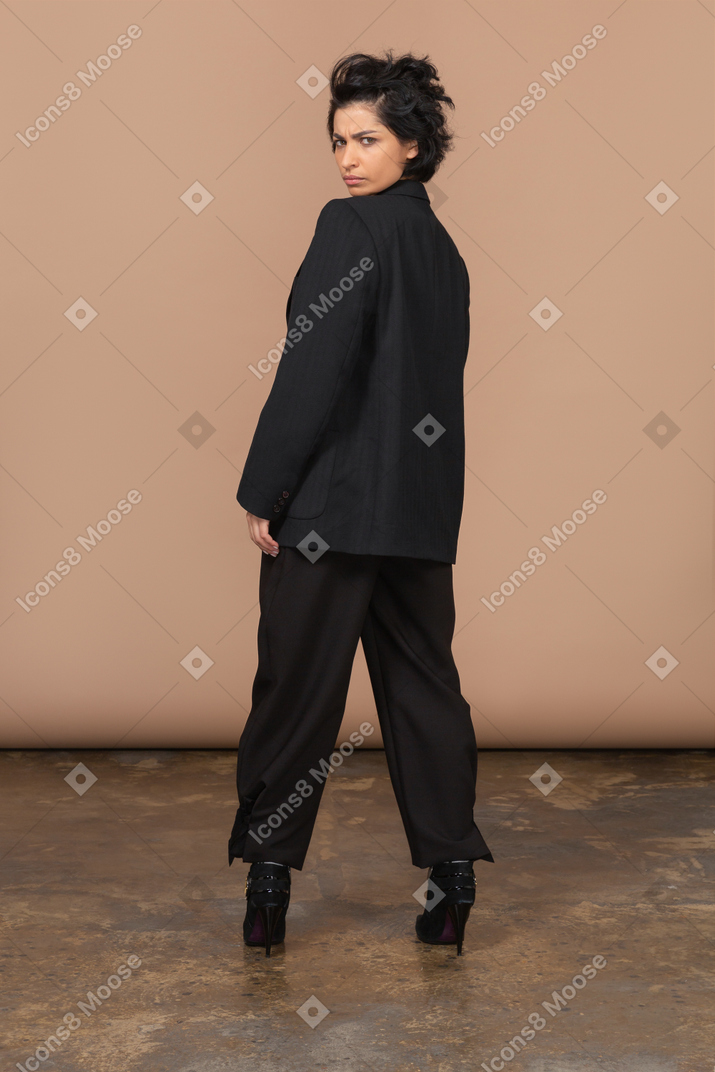 Vista traseira de uma empresária de terno preto tricotando sobrancelhas e olhando para a câmera