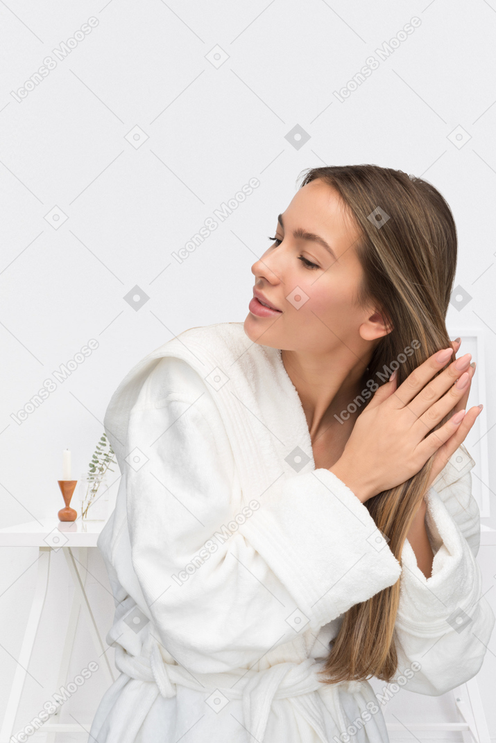 A young woman in a white bathrobe is rubbing her hair