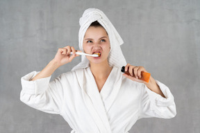 Mujer en bata de baño haciendo muecas mientras se cepilla los dientes
