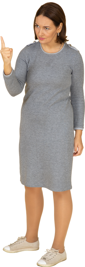 Vista frontal de una mujer en vestido gris apuntando hacia arriba con un dedo