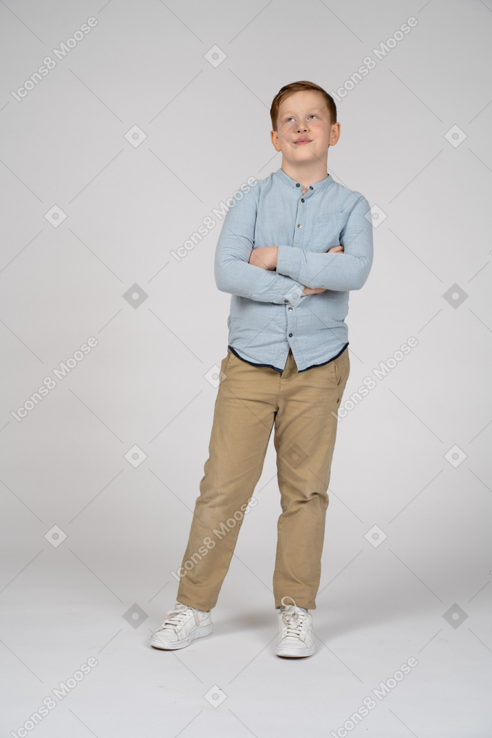 Vista frontal de un niño de pie con los brazos cruzados y mirando hacia arriba