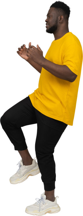 Vista laterale di un giovane uomo dalla pelle scura in maglietta gialla che alza la gamba