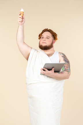 Grande homem caucasiano envolto em toalha segurando sorvete e tablet digital