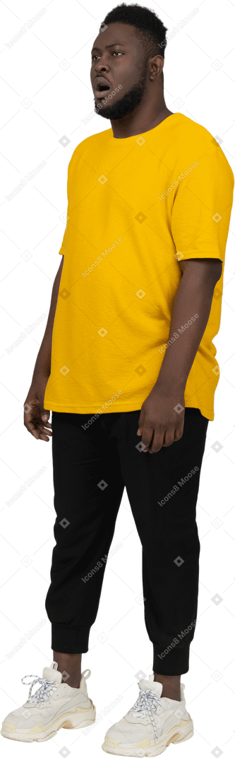 Вид в три четверти удивленного молодого темнокожего мужчины в желтой футболке, стоящего на месте