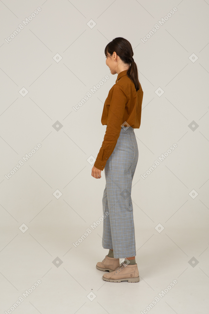 Vista posteriore di tre quarti di una giovane donna asiatica sorridente in calzoni e camicetta