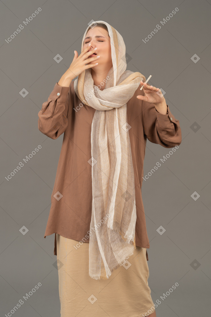 Young woman in headscarf coughing with cigarette in hand