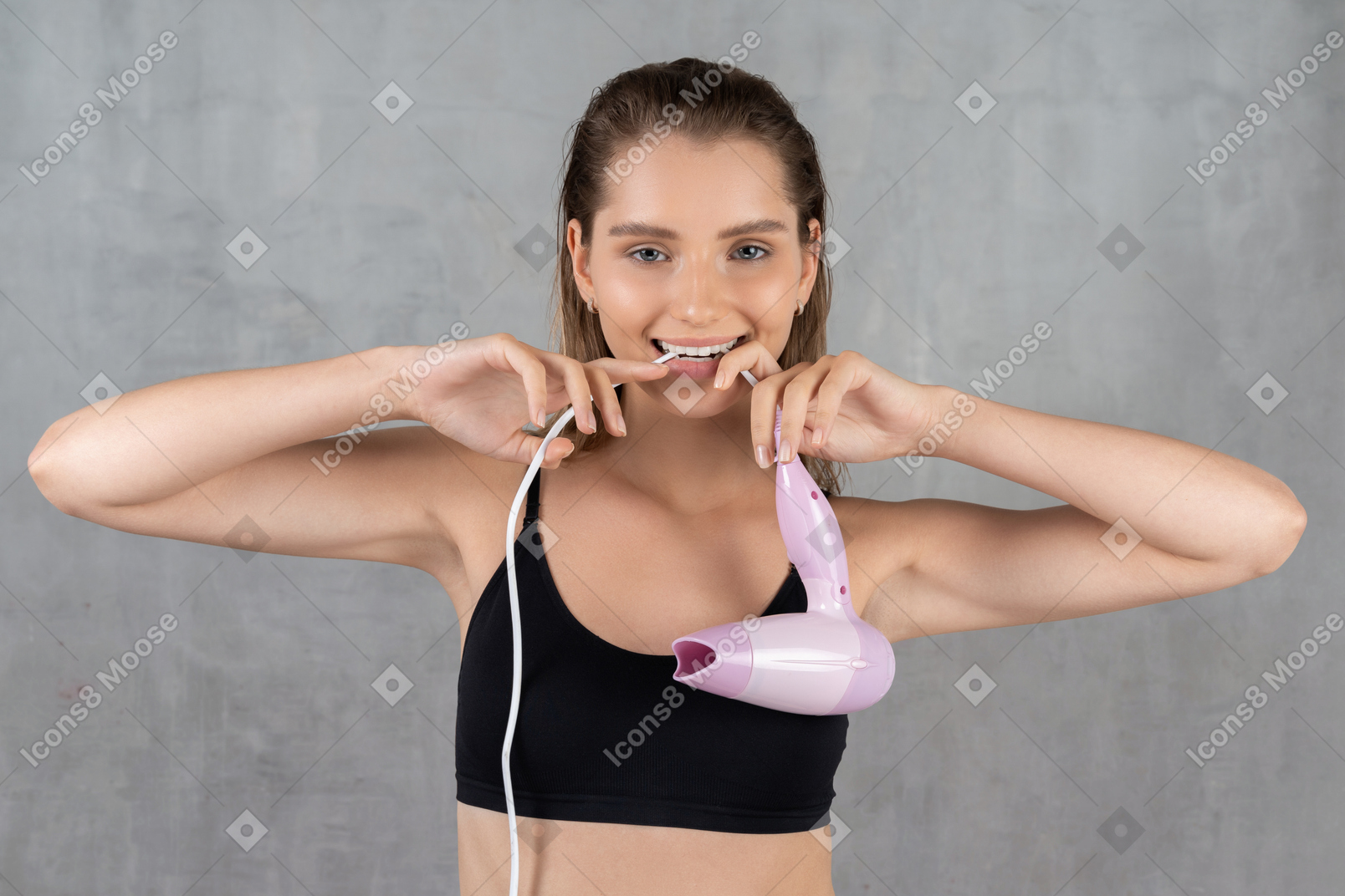 Front view of a smiling young woman biting hairdryer cord