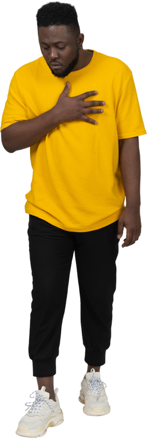 Front view of a surprised young dark-skinned man in yellow t-shirt touching chest