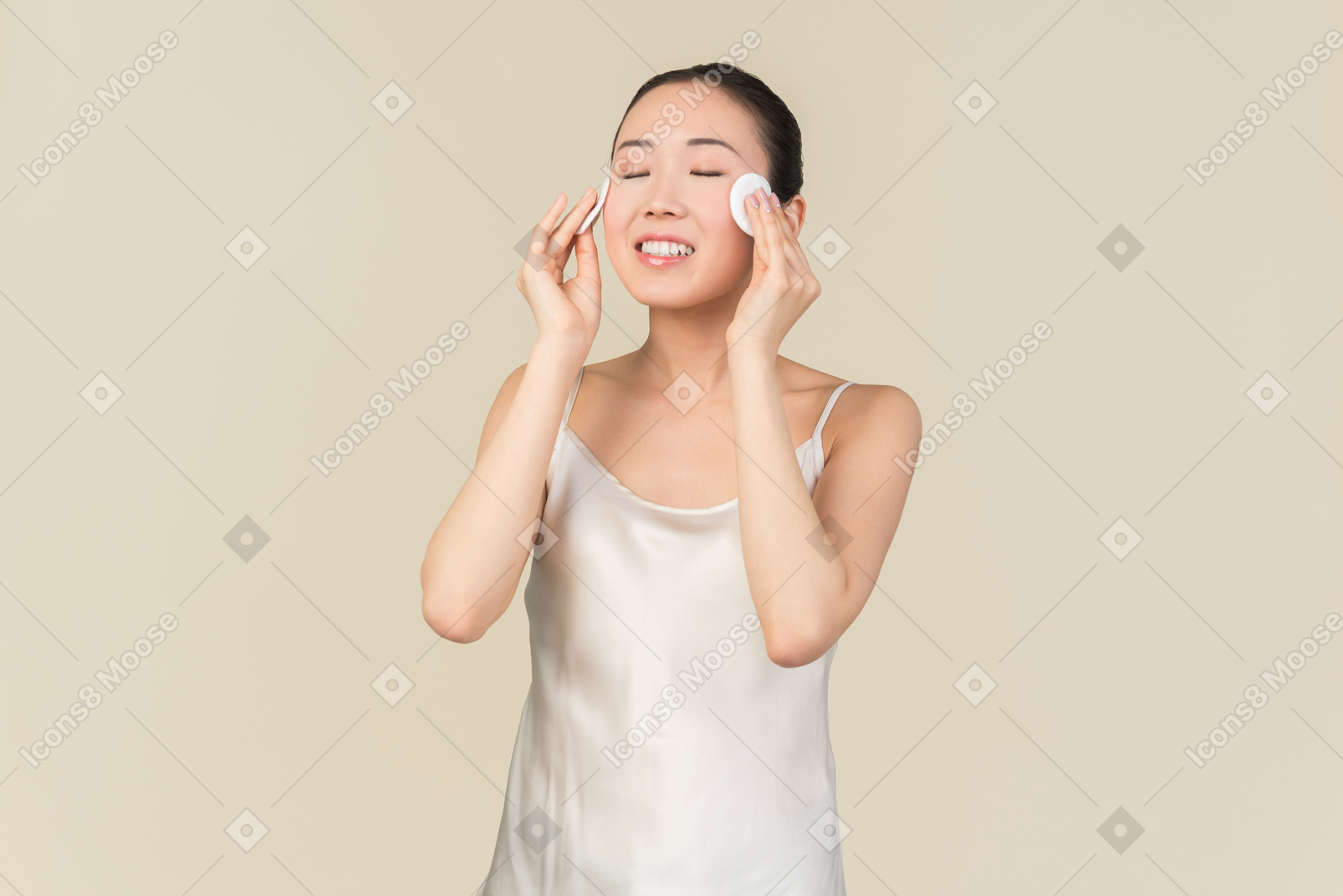 Sonriente joven asiática con los ojos cerrados, limpiando la cara con almohadillas de algodón