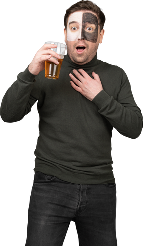 Vista frontal de un fanático del fútbol masculino sorprendido sosteniendo una cerveza