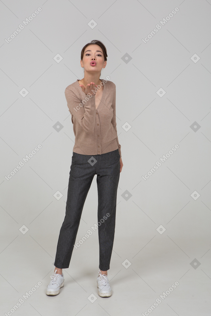 Front view of a young lady in pullover and pants sending an air kiss
