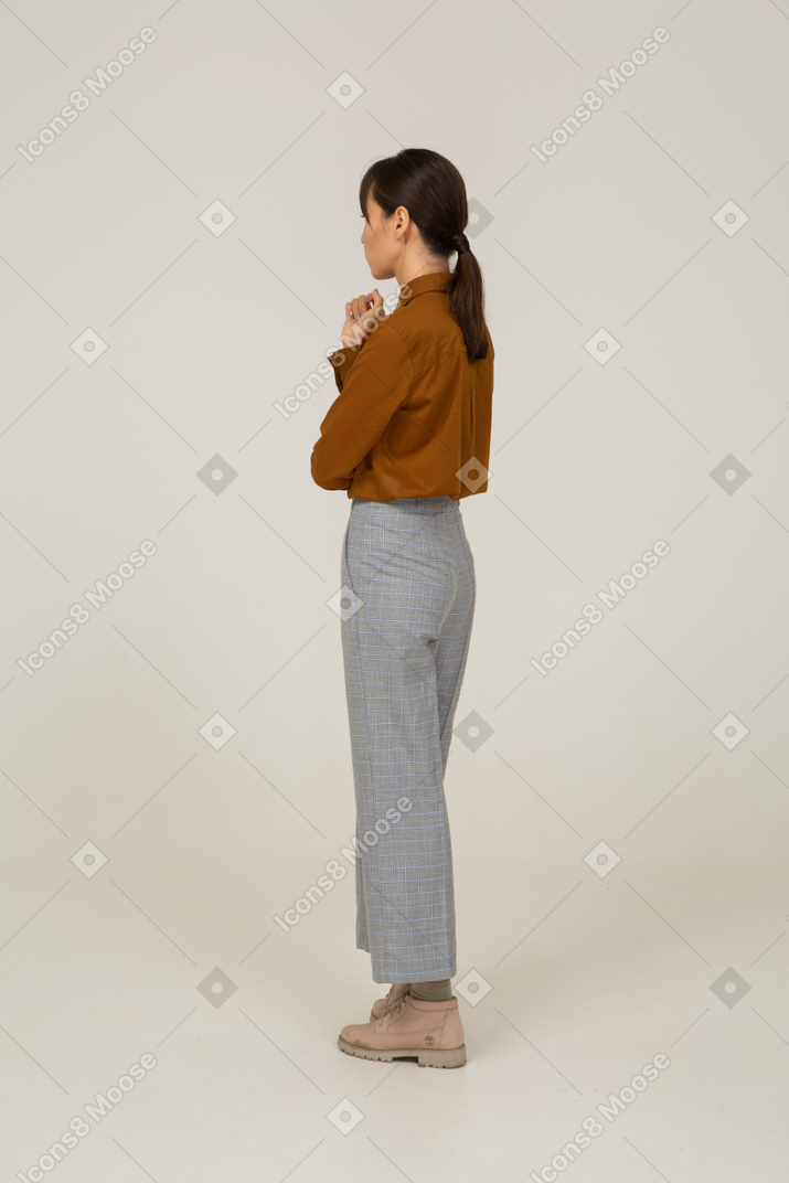 Three-quarter back view of a young asian female in breeches and blouse raising hand