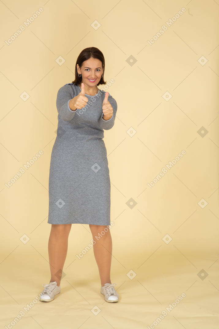 Front view of a happy woman in grey dress showing thumbs up