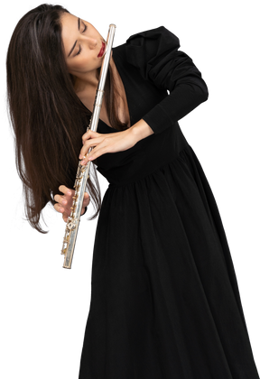 Вид спереди серьезной молодой леди в черном платье, играющей на флейте
