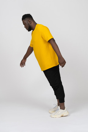 Vista laterale di un giovane uomo dalla pelle scura con una maglietta gialla proteso in avanti e il braccio teso