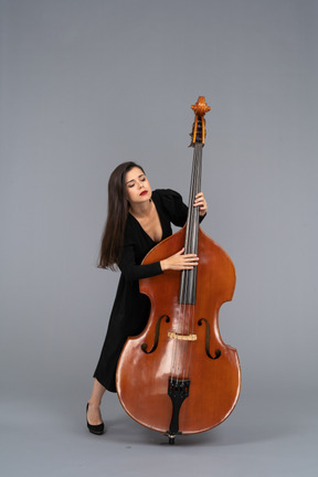 一个年轻的女人，穿着黑色的连衣裙，演奏低音提琴和向前倾斜的前视图