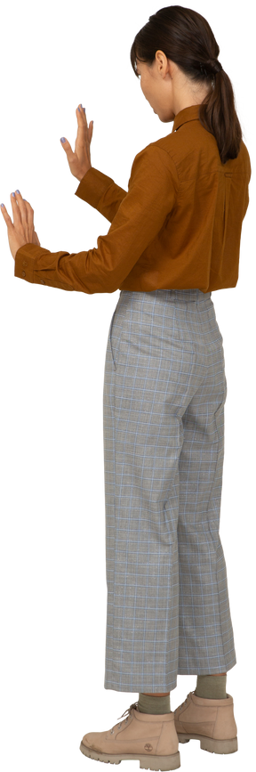 Vista posterior de tres cuartos de una joven mujer asiática en calzones y blusa extendiendo sus brazos