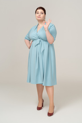 Vista frontal de uma mulher de vestido azul mostrando sinal de ok