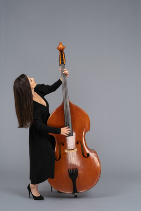 In voller länge einer jungen frau im schwarzen kleid, die kontrabass spielt, während sie sich zurücklehnt