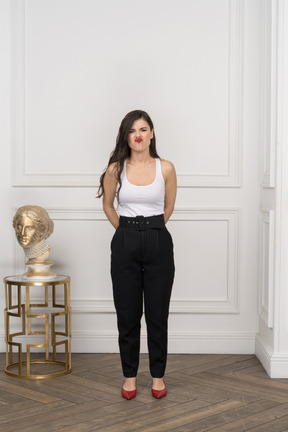 Front view of a grimacing young female holding hands behind while standing near golden greek sculpture