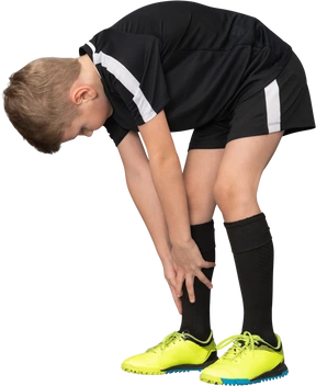 Three-quarter view of a child boy in football uniform leaning forward and touching tiptoes