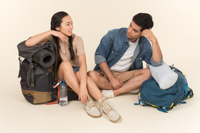 Jovem casal interracial sentado perto de mochilas enormes