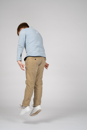 Back view of a boy in a blue shirt jumping and lookign down
