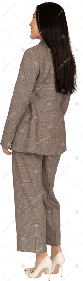 Three-quarter back view of a smiling young lady in brown business suit