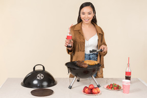 Giovane donna asiatica con bottiglia di coca cola e facendo un barbecue