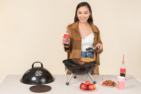 Joven mujer asiática sosteniendo una botella de coca cola y haciendo una barbacoa