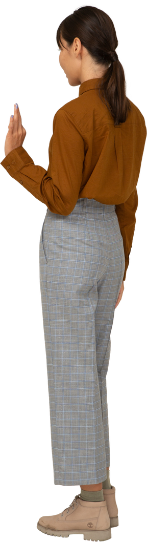 Vista posteriore di tre quarti di una giovane donna asiatica in calzoni e camicetta che mostra gesto ok