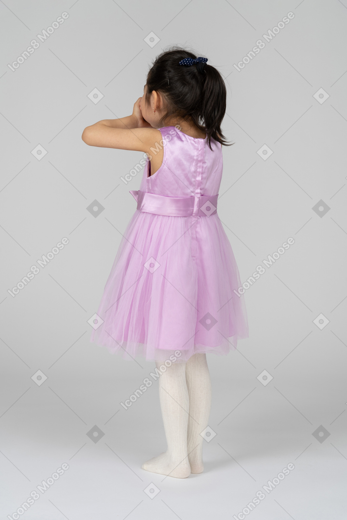 Girl in a pink dress closing her mouth with hands